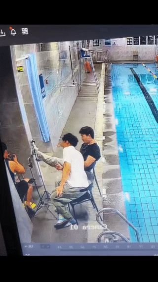 两名男子正坐在游泳池边上直播？
结果其中有一名黑衣男子突然翻进旁边的游泳池里？