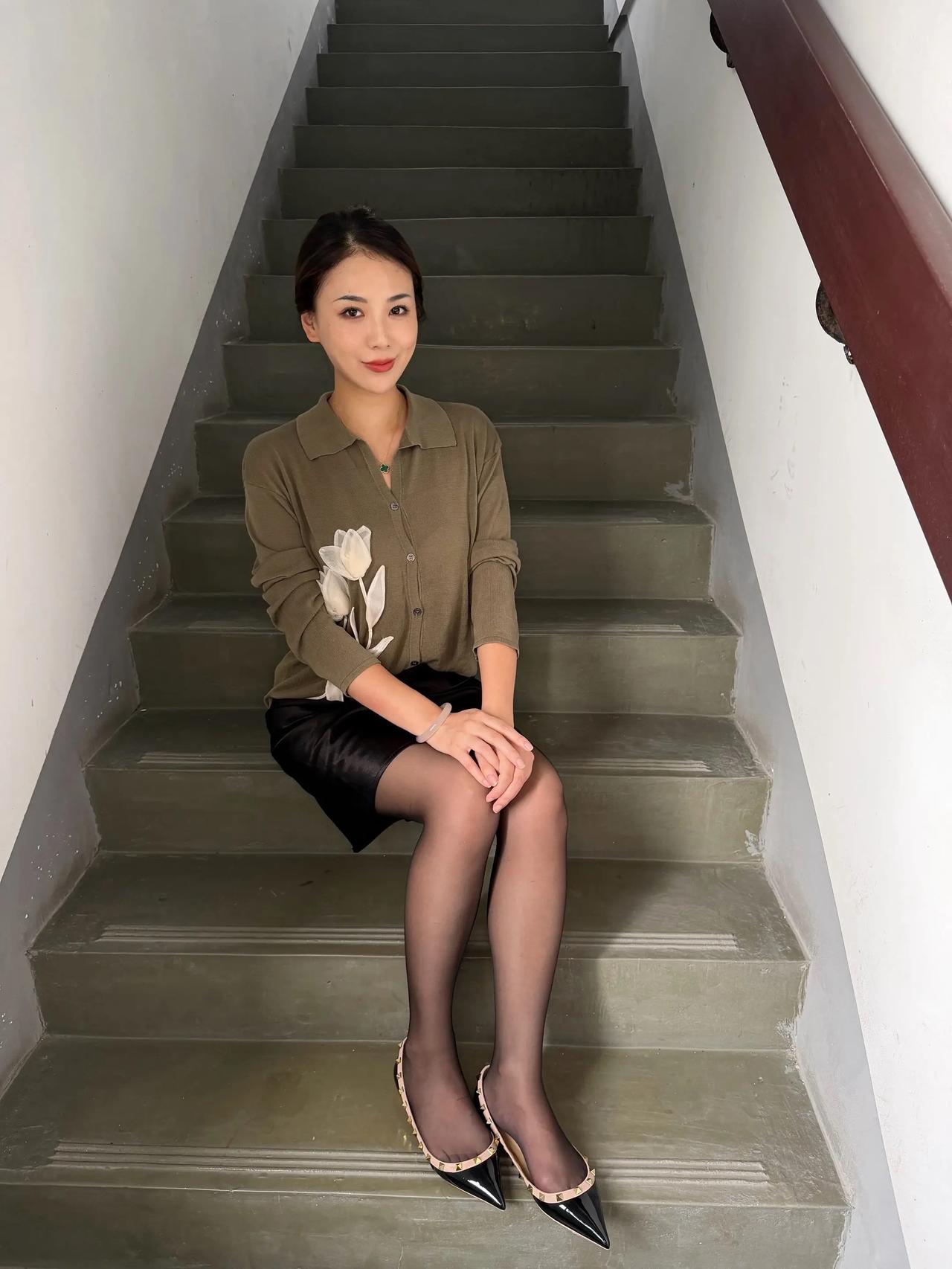这姑娘坐在楼梯上，穿着高跟鞋。
