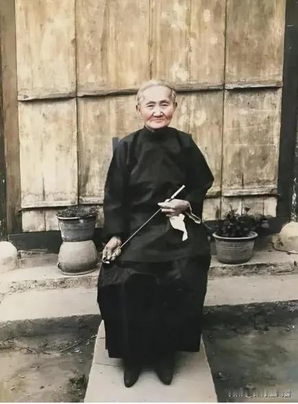 这张照片拍摄于解放前的白区，是一位地主婆在家门前的留影。白发花白的她梳着背头，双