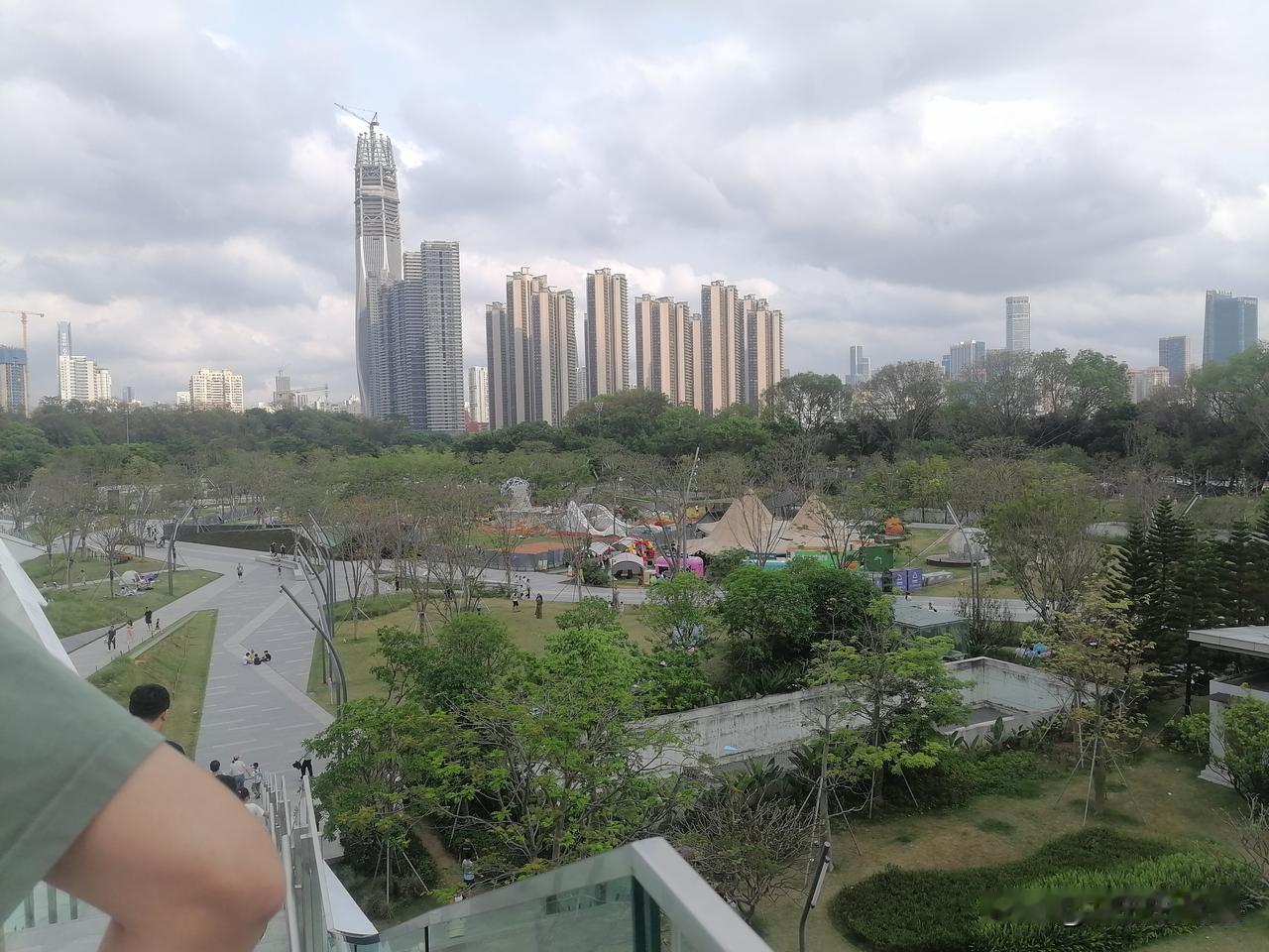 远处大楼高耸入云，有的还在紧张施工中，近处公园一角，有人在游玩！