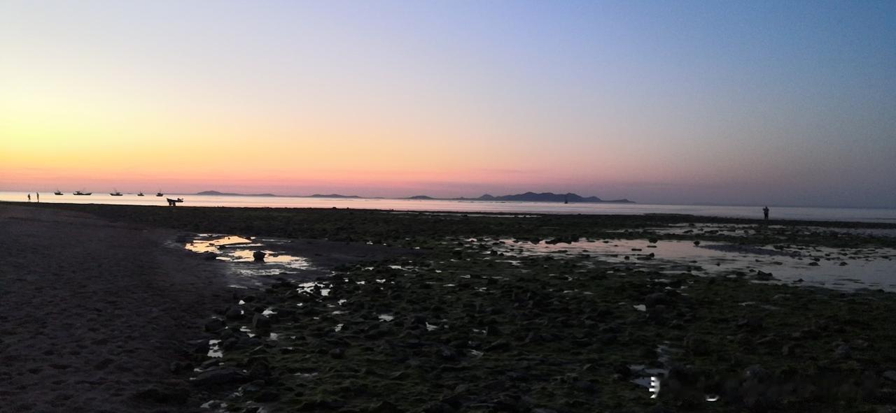 夕阳下的大海，就像被打翻了调色盘，海面和天空被染成了七彩斑斓的颜色。海边的人们如