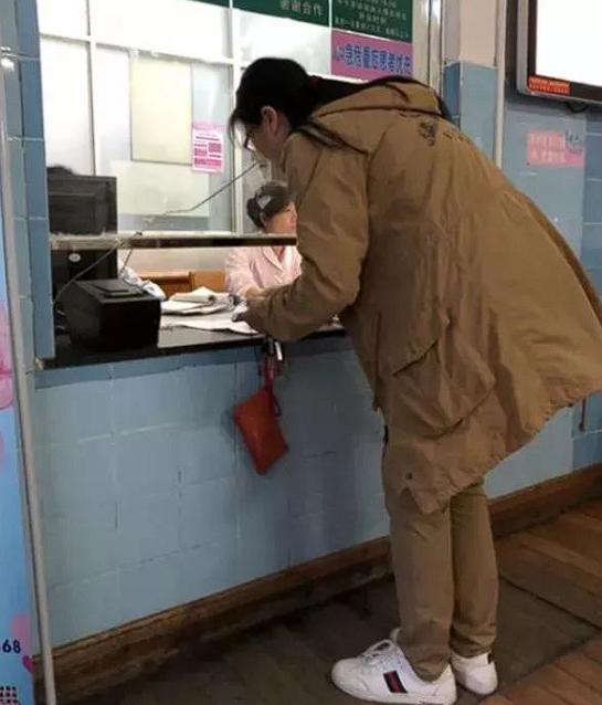 广东，一名孕妇站在医院的收费窗口前，一手紧攥着缴费单，一手摸着已经鼓起的肚子，脸