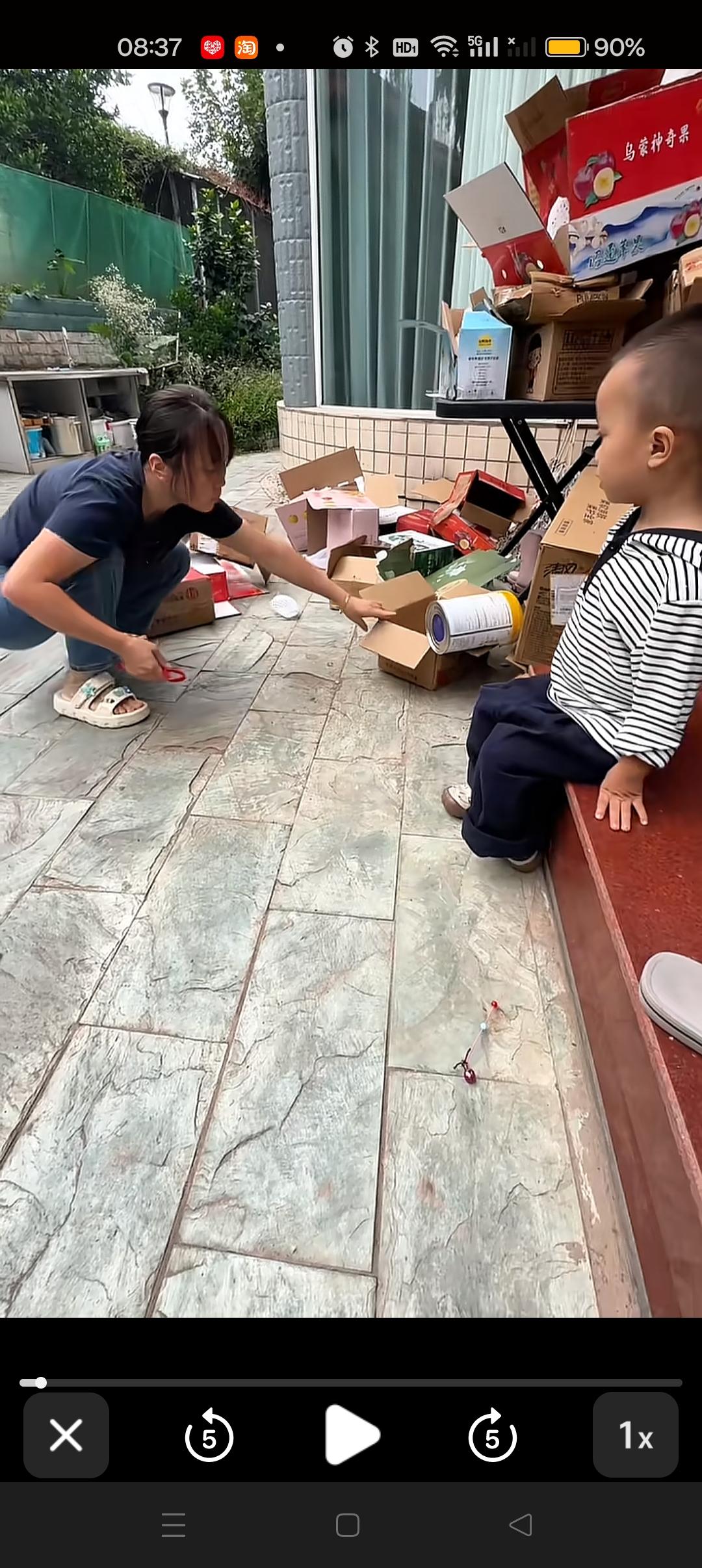 甘宇翼老婆在整理自家的废纸箱，打包好，这样就可以卖点零食钱了，儿子在旁边默默的陪