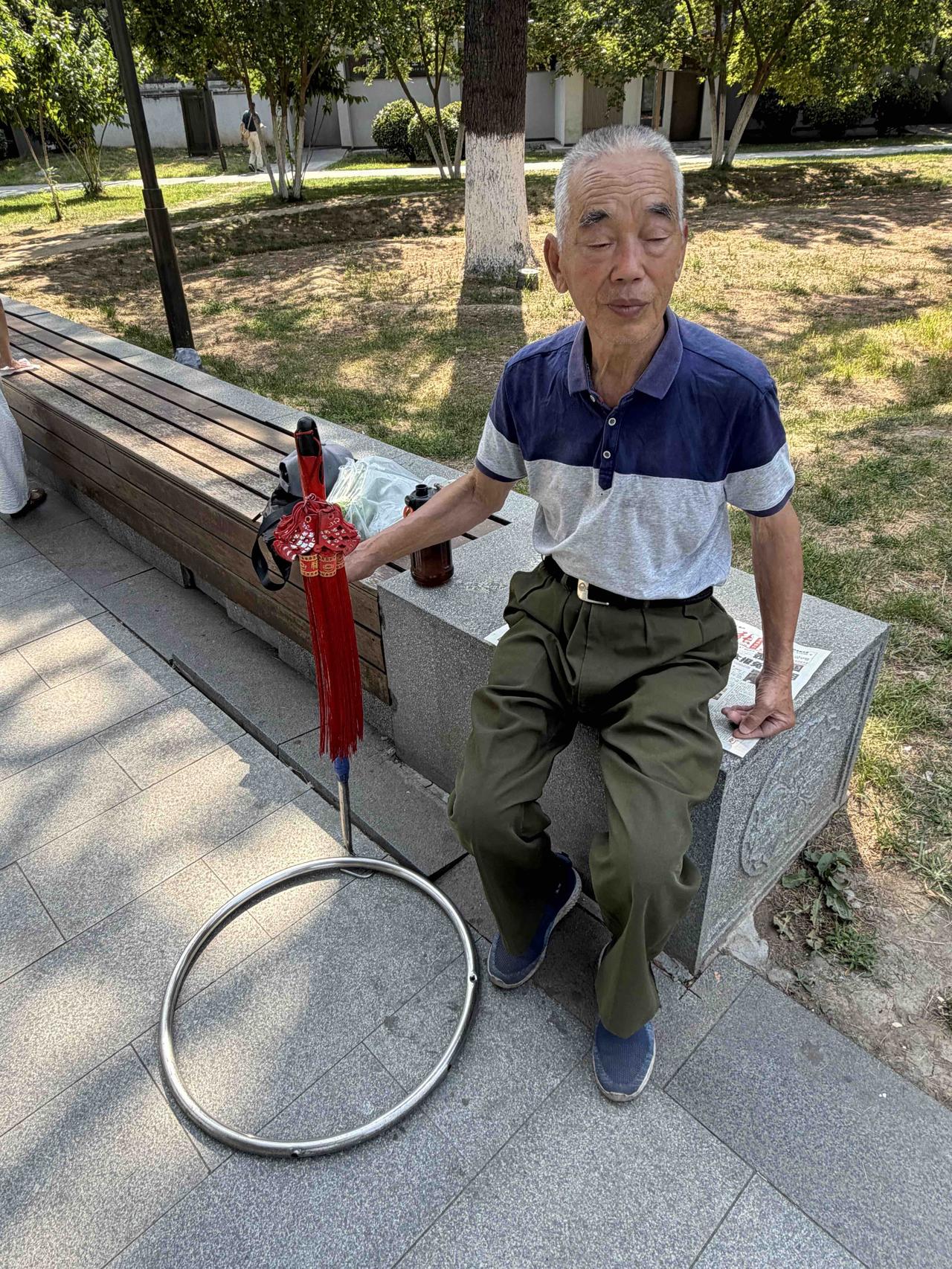 前天上午，我逛西安兴庆宫公园，看到一位坐着歇息的老者，脚下放着一个大铁环，旁边立