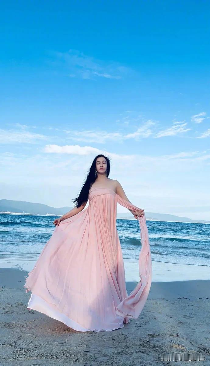 钟丽缇在社交平台晒出一组海边美照，她身穿一袭粉色抹胸裙，光着脚丫在海边悠闲漫步，