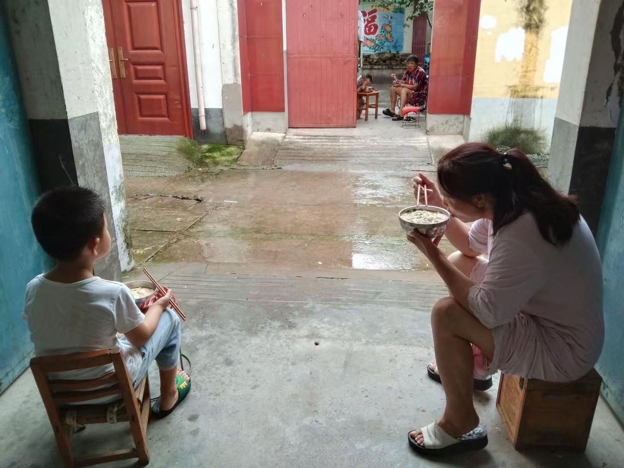 前不久一个中午，路过一农村的小街巷，看到两家对门，两个奶孙俩分别坐在自家门洞下，
