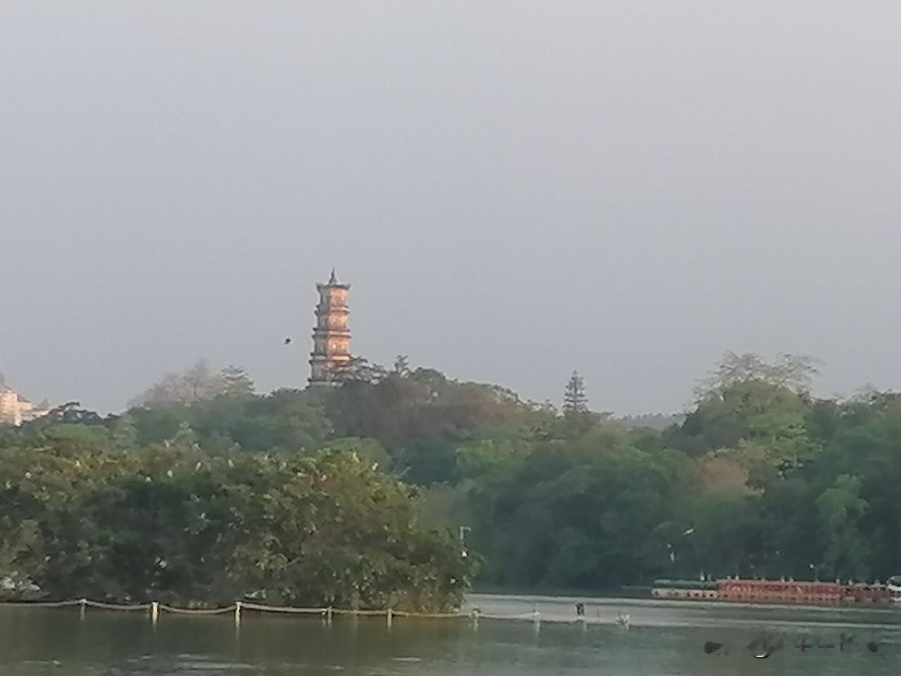 雄伟壮观的古塔屹立西湖山上，湖边古朴大气的亭台楼阁星罗棋布，几处有小孩在玩水炮，