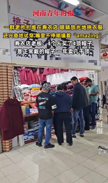 10月20日，江苏镇江，一群老外扎堆在寿衣店门口挑选衣服，看着墙上挂的衣物他们眼