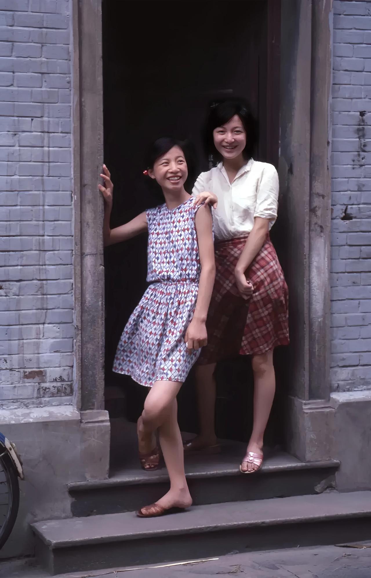 上个世纪80年代，两个美少女站在家门口拍摄的一张合影。
她们笑得好灿烂。
