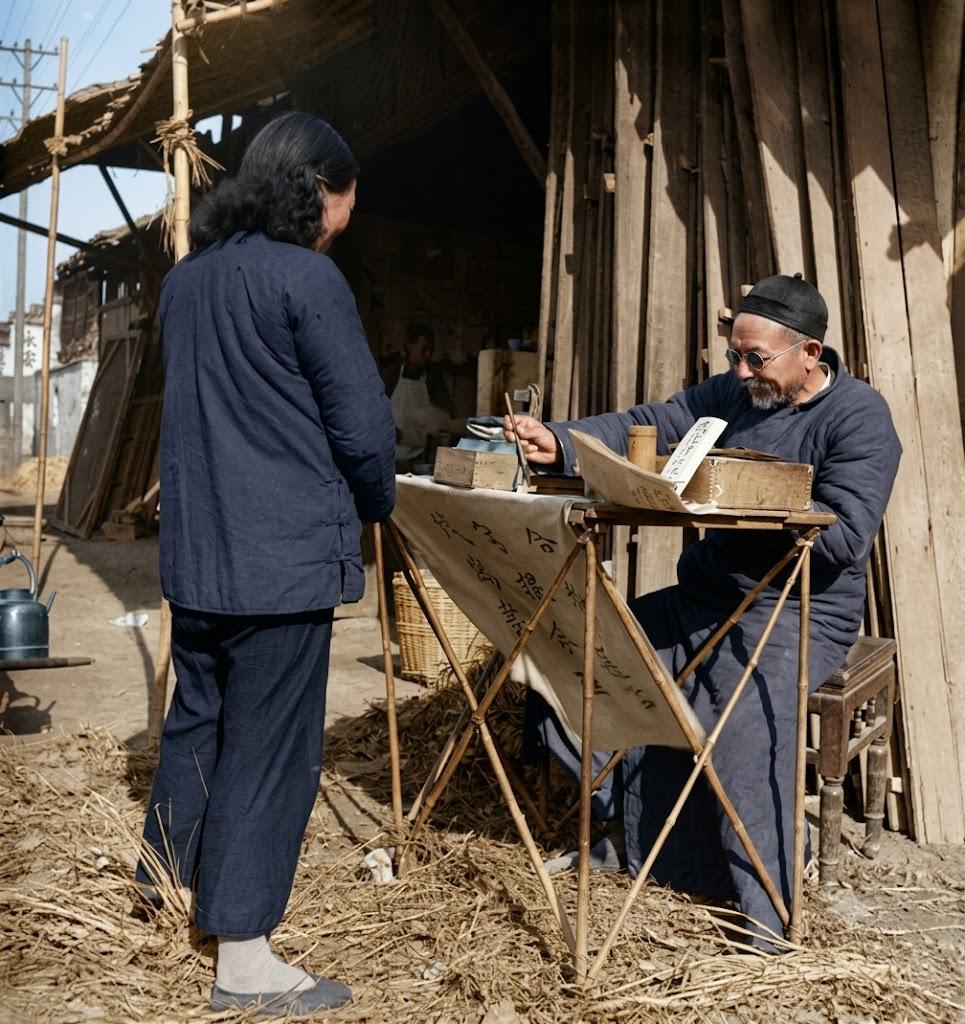 1940年，南京街头的代写信小摊。戴瓜皮帽的老先生架着老花镜，端坐在折桌后，面前