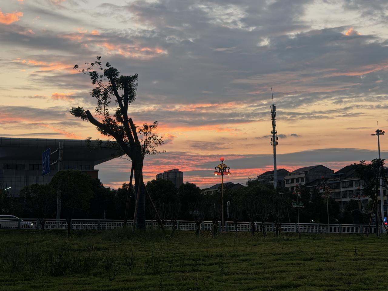 落日漫过城市楼宇，橘红晚霞铺满天边。
车来人往的街道，灯火次第亮起，平凡小城的黄