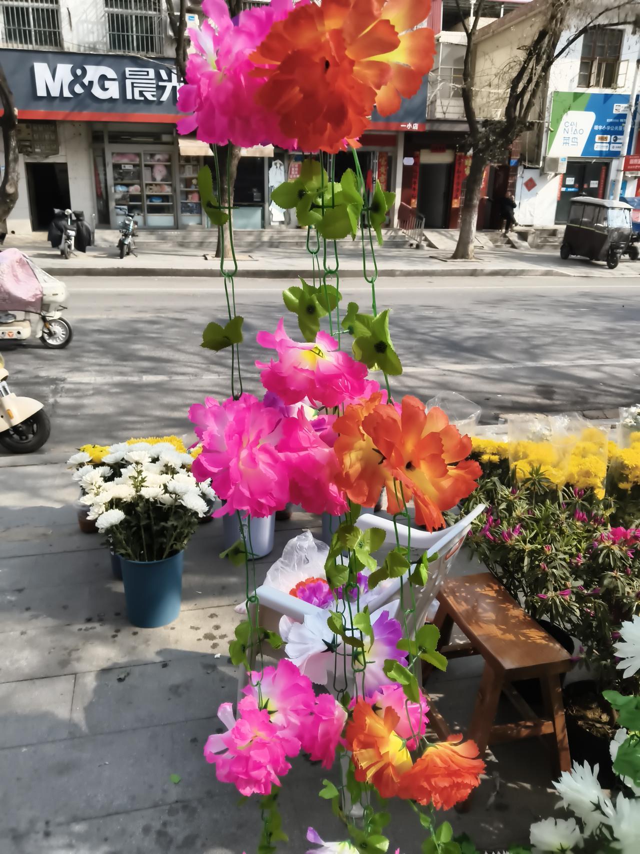 垂挂的仿真牡丹开得热烈，玫红与橘红的花瓣层层叠叠，在风里轻轻晃着，衬得翠绿的藤蔓