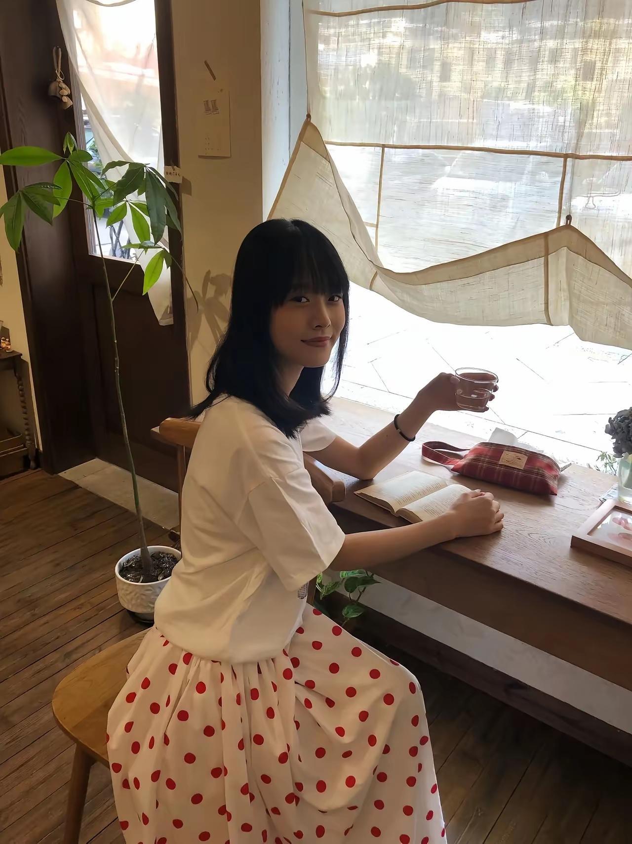 女孩在窗边看书，喝着饮料。