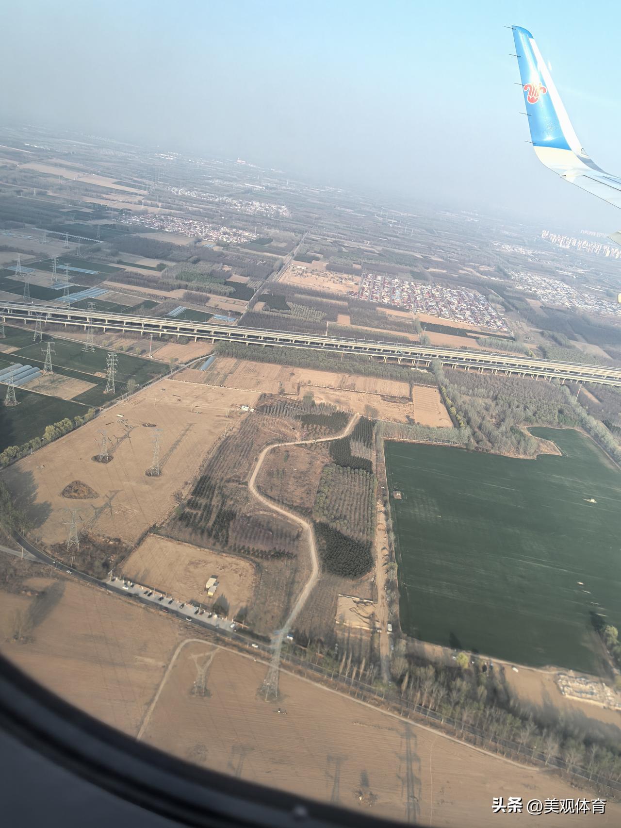 飞机上清晰可见平行的高速公路和铁路，以及村庄、农田、输电线等地物。