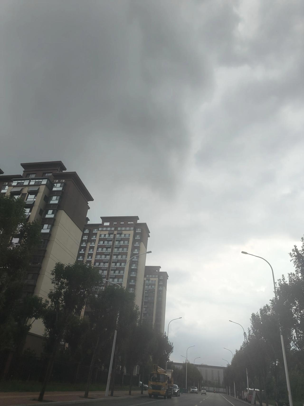 阴云密布的城市街景，行人匆匆，车辆穿梭。下午1:30，鲁西南济宁兖州区乌云密布，