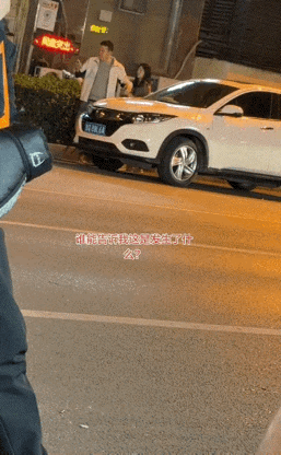 街上一幕，白衣男子右手拿着手机聚精会神看着，左侧一位身材苗条的年轻女士，拼命拉拽