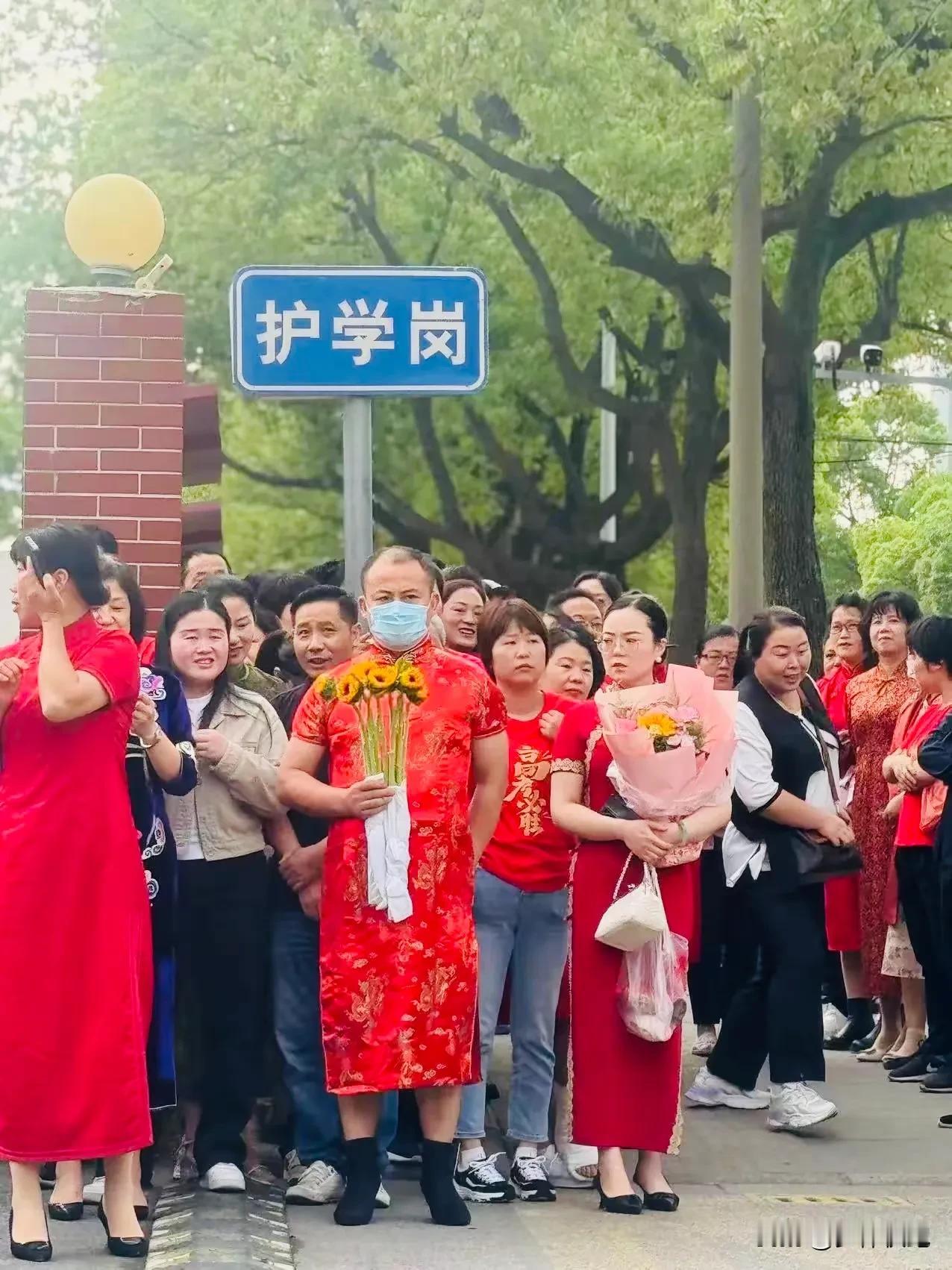 高考考场外，一位男家长穿着红旗袍，手握向日葵，不出意外的话极有可能还是紫色内裤（