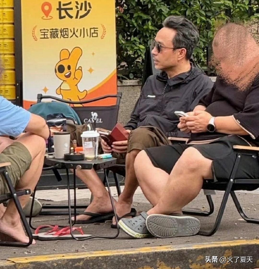 52岁汪涵在街头坐着和朋友聊天，穿着人字拖吃着槟榔，用着三折叠手机，头发两侧都白