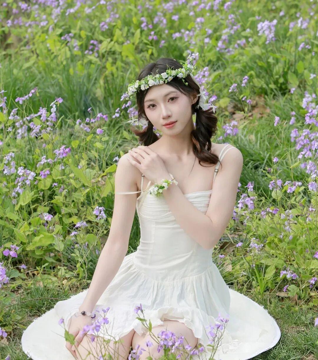 她身着一袭纯白吊带纱裙，轻盈的裙摆如云朵般铺散在草地上，简约的设计勾勒出纤细优美