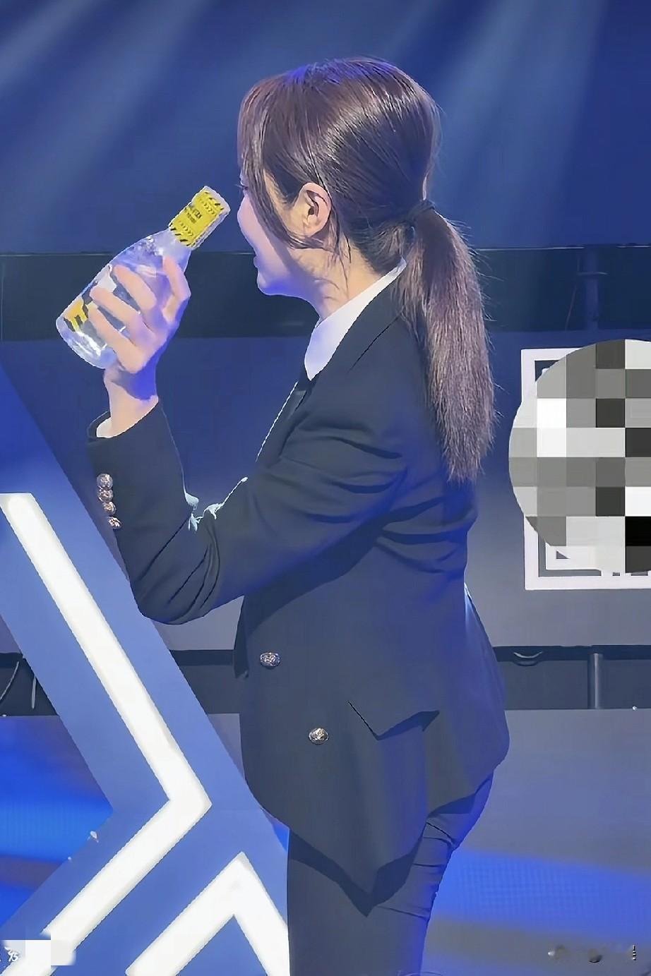 在舞台的聚光灯下，王钟瑶一身干练的黑色西装，马尾利落，手持水瓶