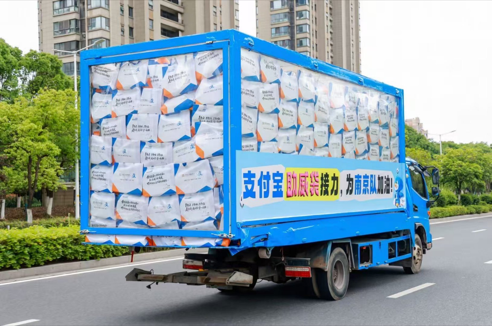 苏超助威袋坐着卡车来南京了南京全城开启巡游派送，透明卡车满载十万份苏超助威 袋，