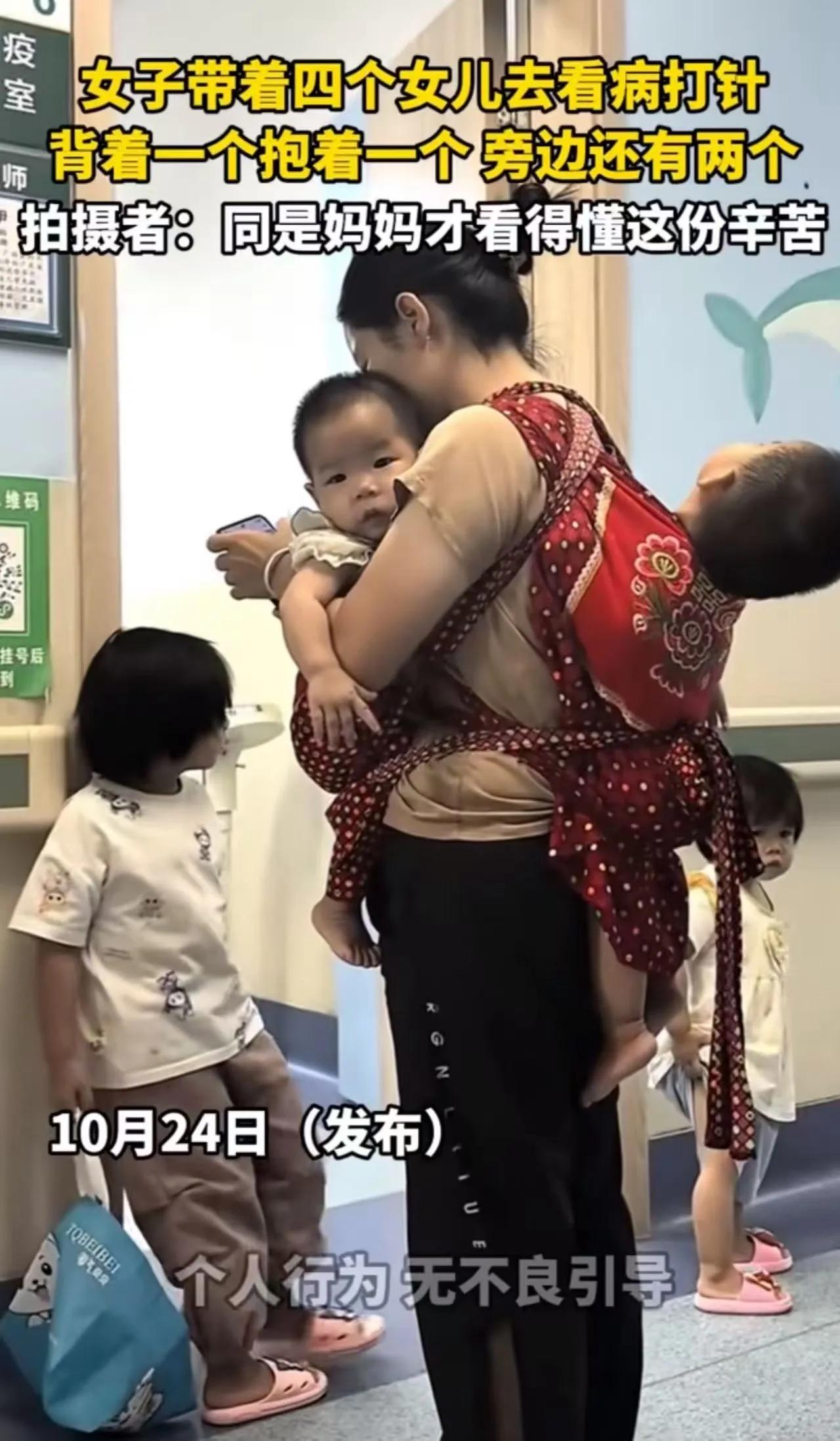 医院走廊里，一个年轻妈妈背着最小的，怀里兜着另一个，脚边还杵着两个小姑娘。四个人