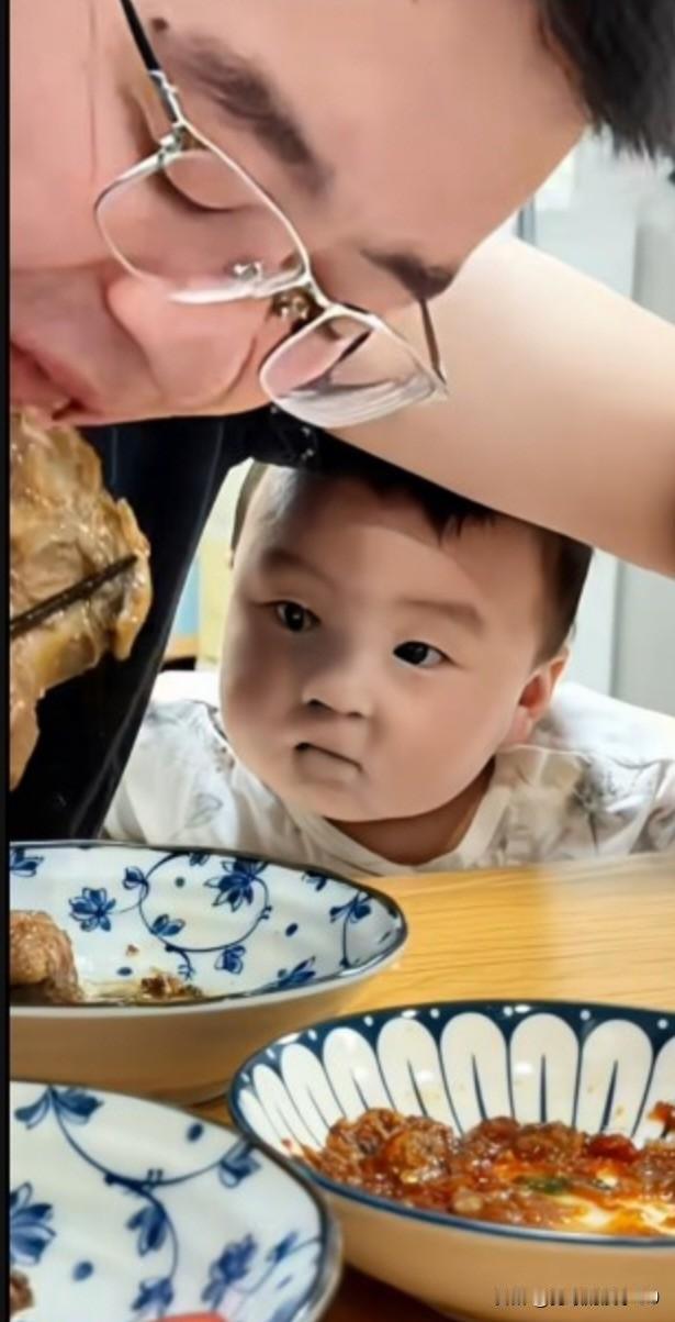 这一幕令人心酸。父亲只顾大快朵颐地啃着猪蹄，没留意趴在桌上的小孩，那清澈眼神中对