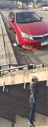 一名男子悬挂在埃及舒卜拉海马的马扎拉特桥上，旁边停着一辆红色比亚迪汽车。警察和救