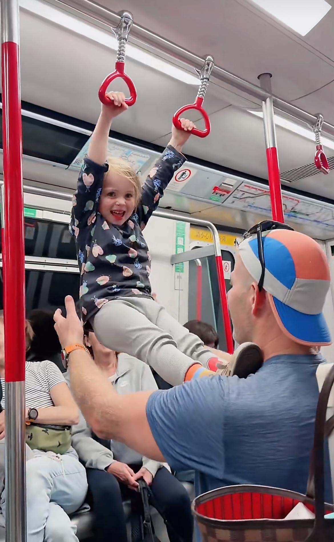 港铁上，一个白人小孩在地铁玩吊环，想在游乐园里面玩得真开心