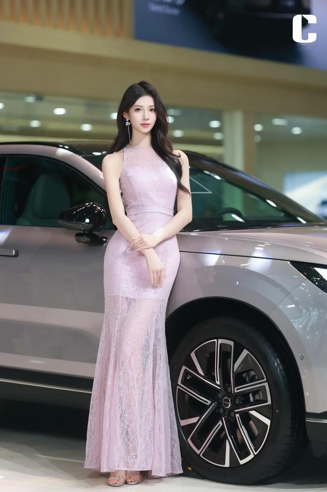 《车展上的粉色焦点》
在车展的璀璨灯光下，一位身着粉色连衣裙的女模特成为了全场瞩