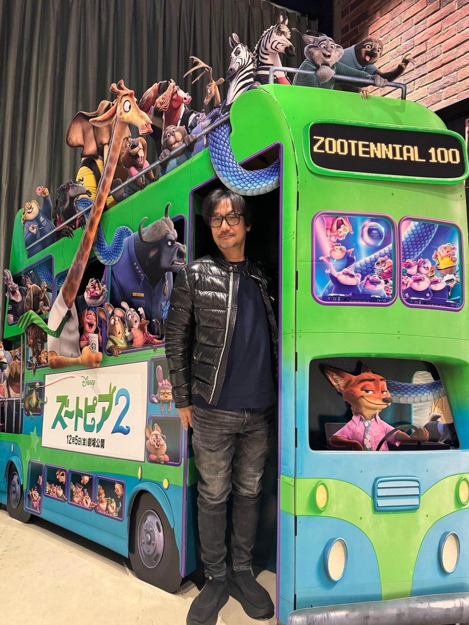 小岛秀夫和《疯狂动物城2》的海报合影，他要给鼹鼠警官保罗配音疯狂动物城跨年电影愿