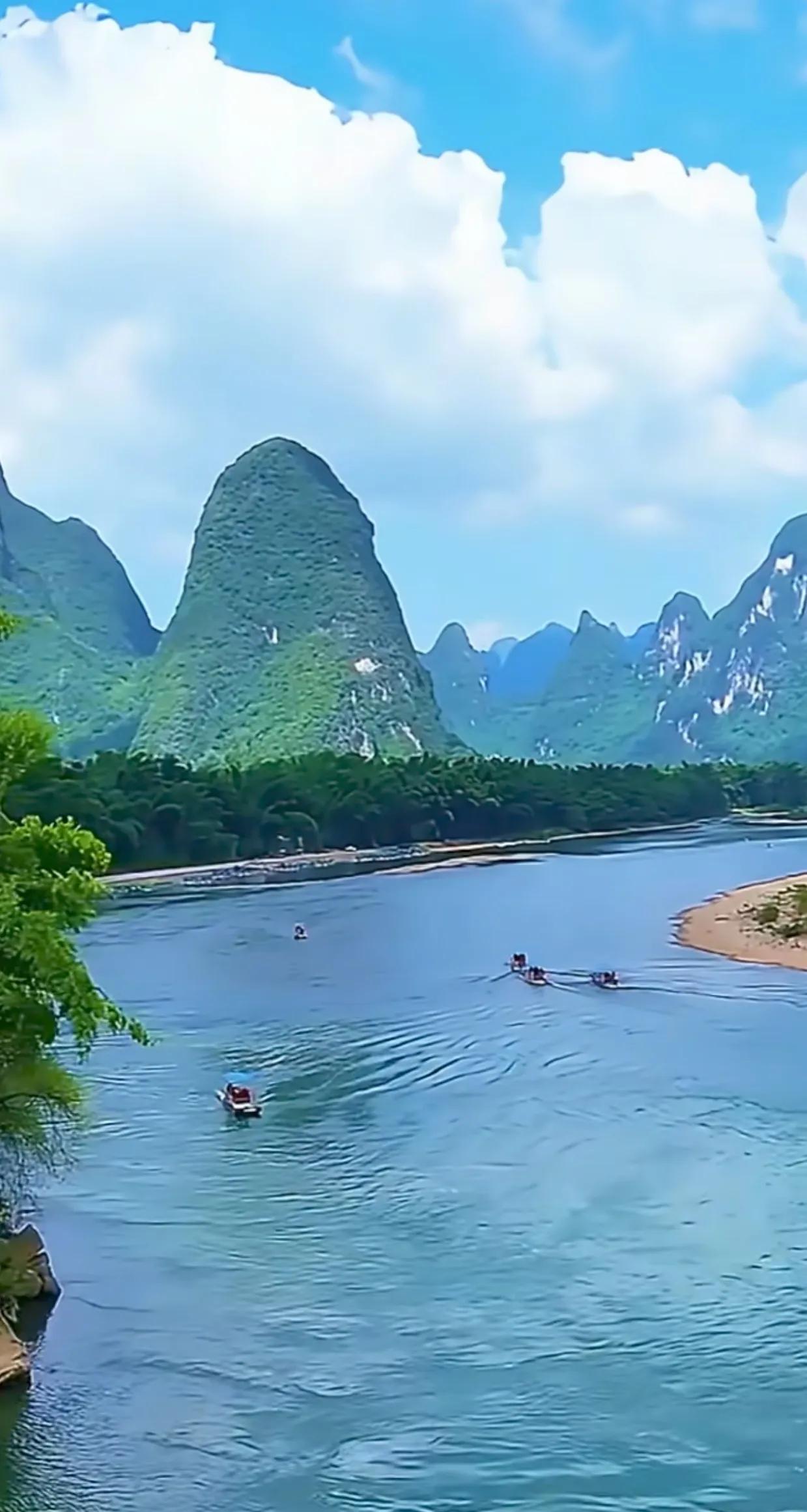 峰峦巍峨，江水潺潺，绿树掩映下的小船，宛如诗行般缓缓前进，让人沉醉于这静谧而美好