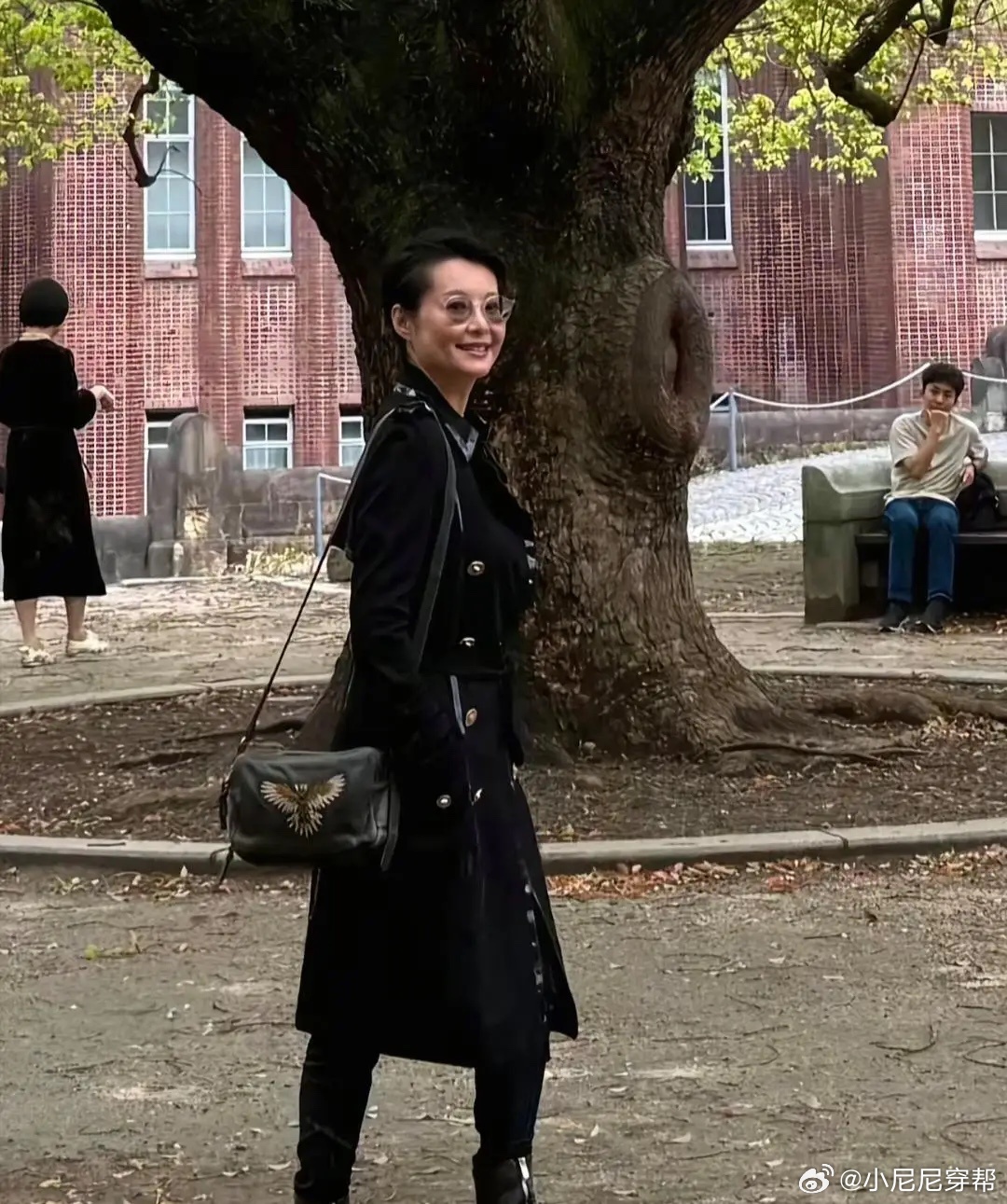 54岁袁立和老公梁太平在日本东京大学内赏樱花，她身穿黑色长大衣，背着名牌包，身材