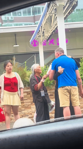 一个老外正在街头和一名中国女子约会。
在他们旁边竟然还站着一位卖花的老奶奶？
老