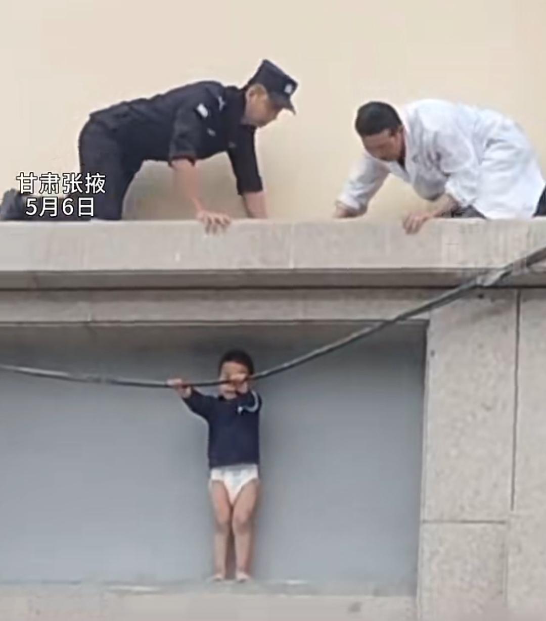 甘肃张掖的一栋居民楼外，4岁男童不慎翻出窗户，被困在两层楼之间的狭窄平台上，下方
