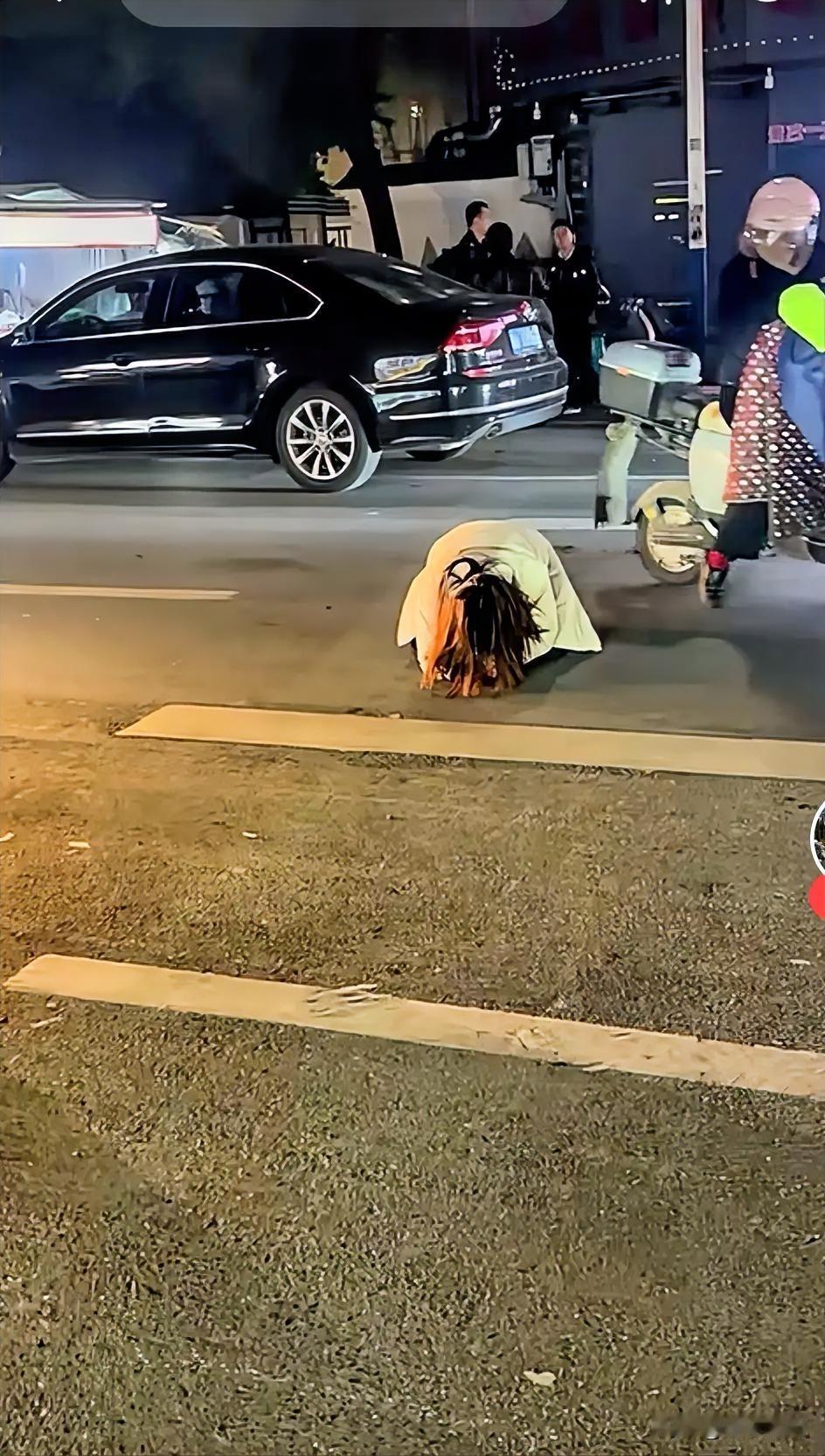 一名女子跪在马路中央撕心裂肺的痛哭着，路人都不由的望向该名女子，而不远处几米的位