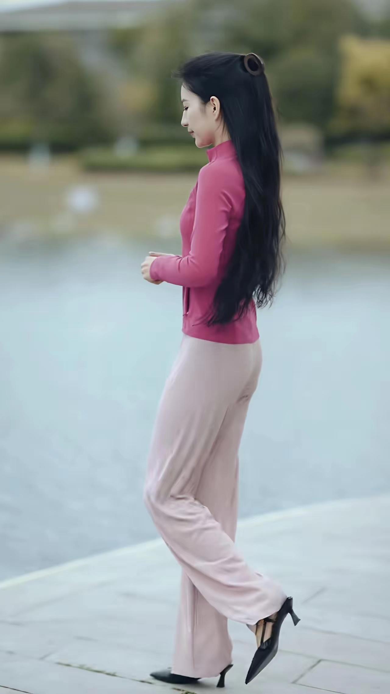 一位女士穿着粉色套装在湖边散步。