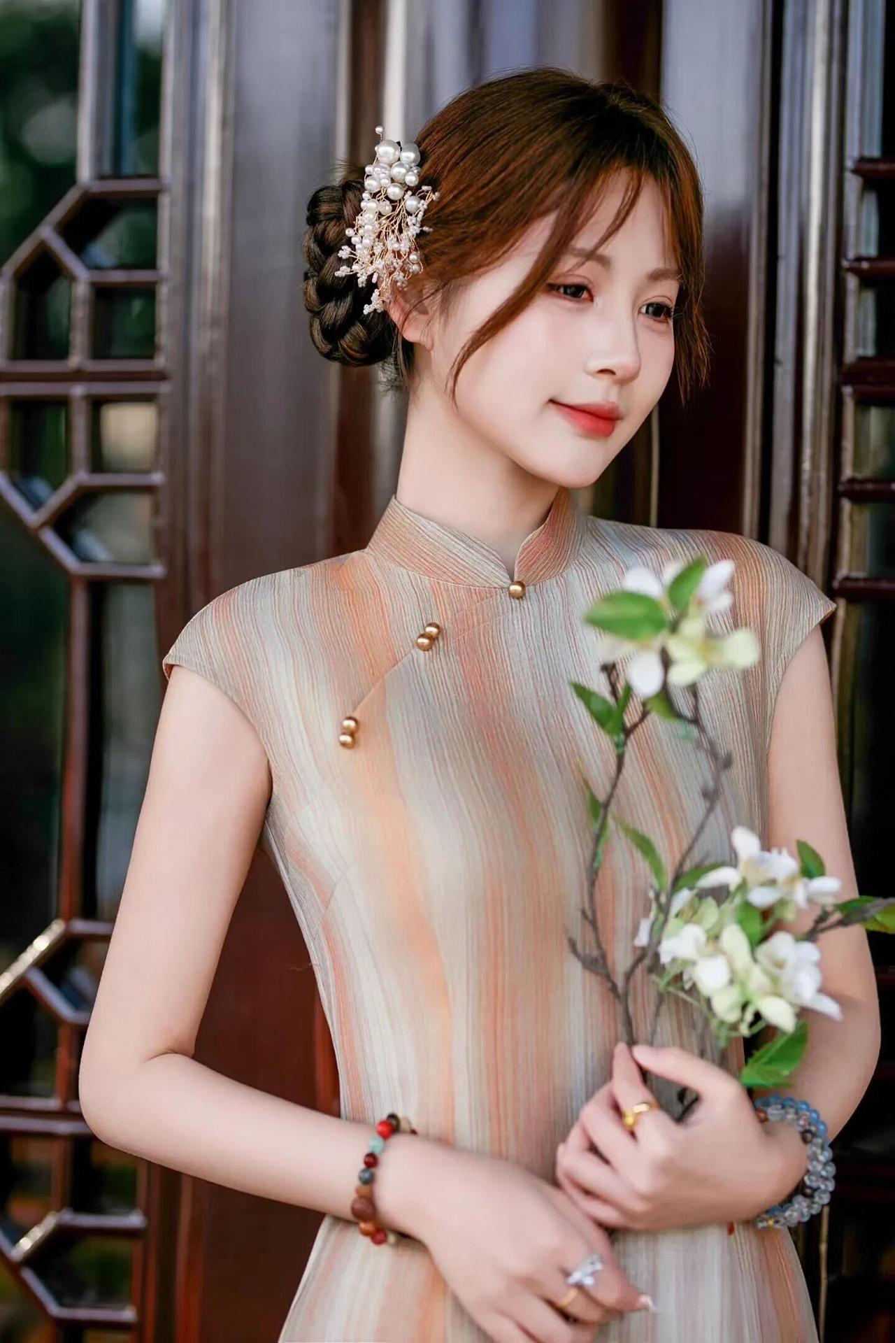 她的发型精致，发髻上点缀着珍珠与花枝发饰，增添了几分灵动与贵气。手持一束素雅的白