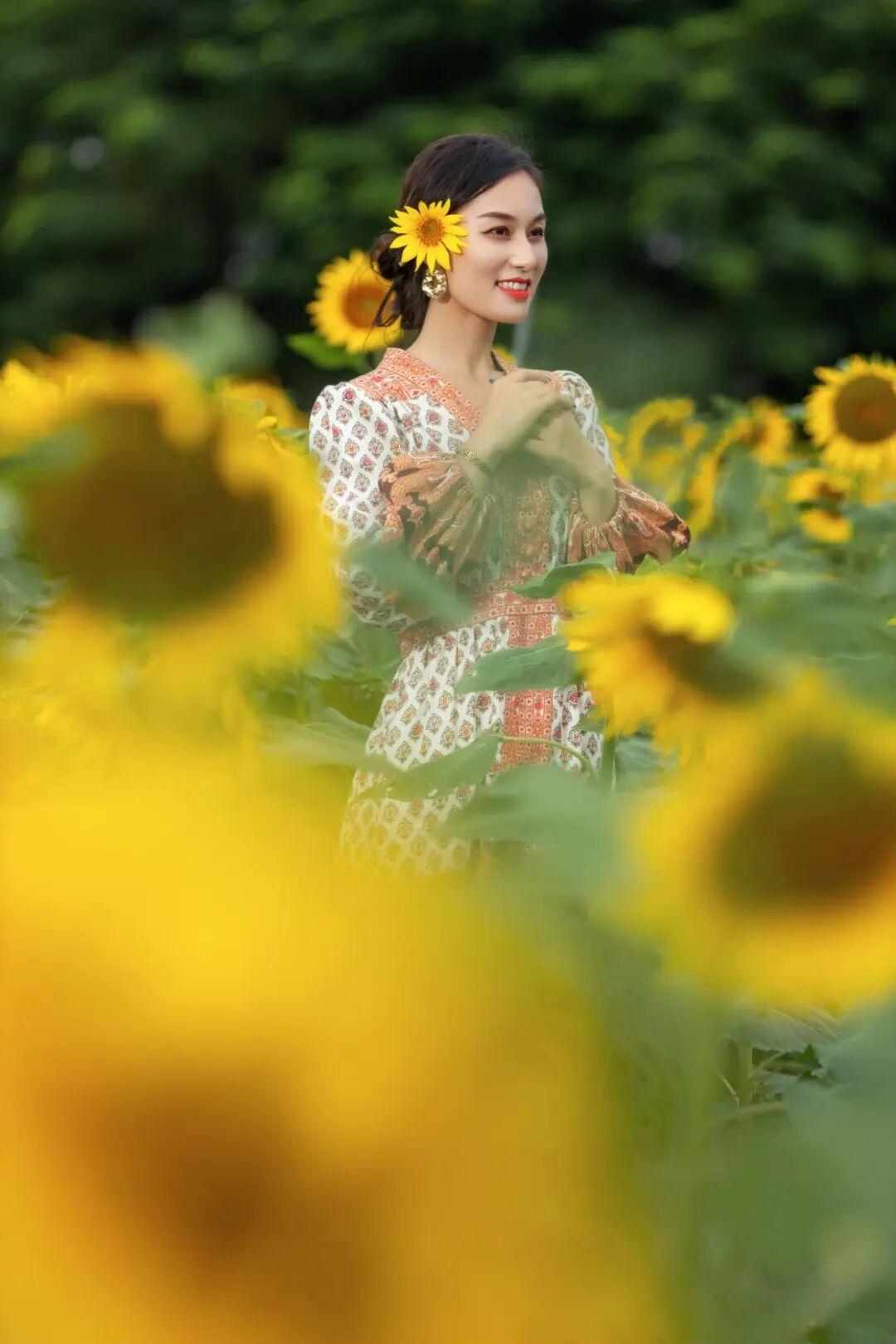 在广袤的向日葵花田中，一位女性静静地站立着。她穿着一件带有精致花卉图案的白色长袖