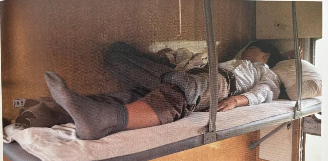80年代的列车硬卧的上铺，一位旅客正惬意打盹。他穿着长袖衣裤，脚上是那时男士夏天