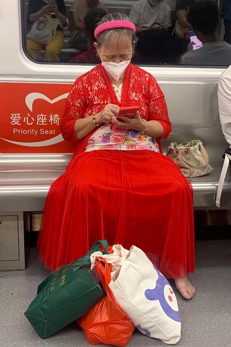 地铁偶遇一幕，看着有点一言难尽！
爱心座位上坐着一位穿搭鲜艳的大妈，一身红色长裙