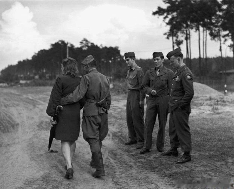 1945年，柏林，一名苏联士兵搂着德国女人从美国兵面前走过US troops w