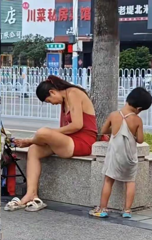 35℃高温，徐州街头的绿化树下，一对母女已经住了半个月。
母亲穿着红色连衣裙，头