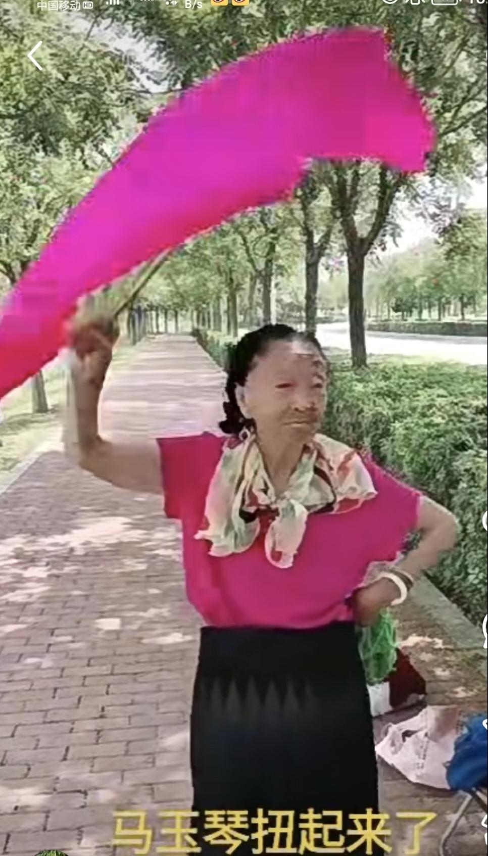粉色短袖，黑色半身裙，花色丝巾一系，脚踩绣花鞋，左手拿着绿色手帕，右手执着粉色扇