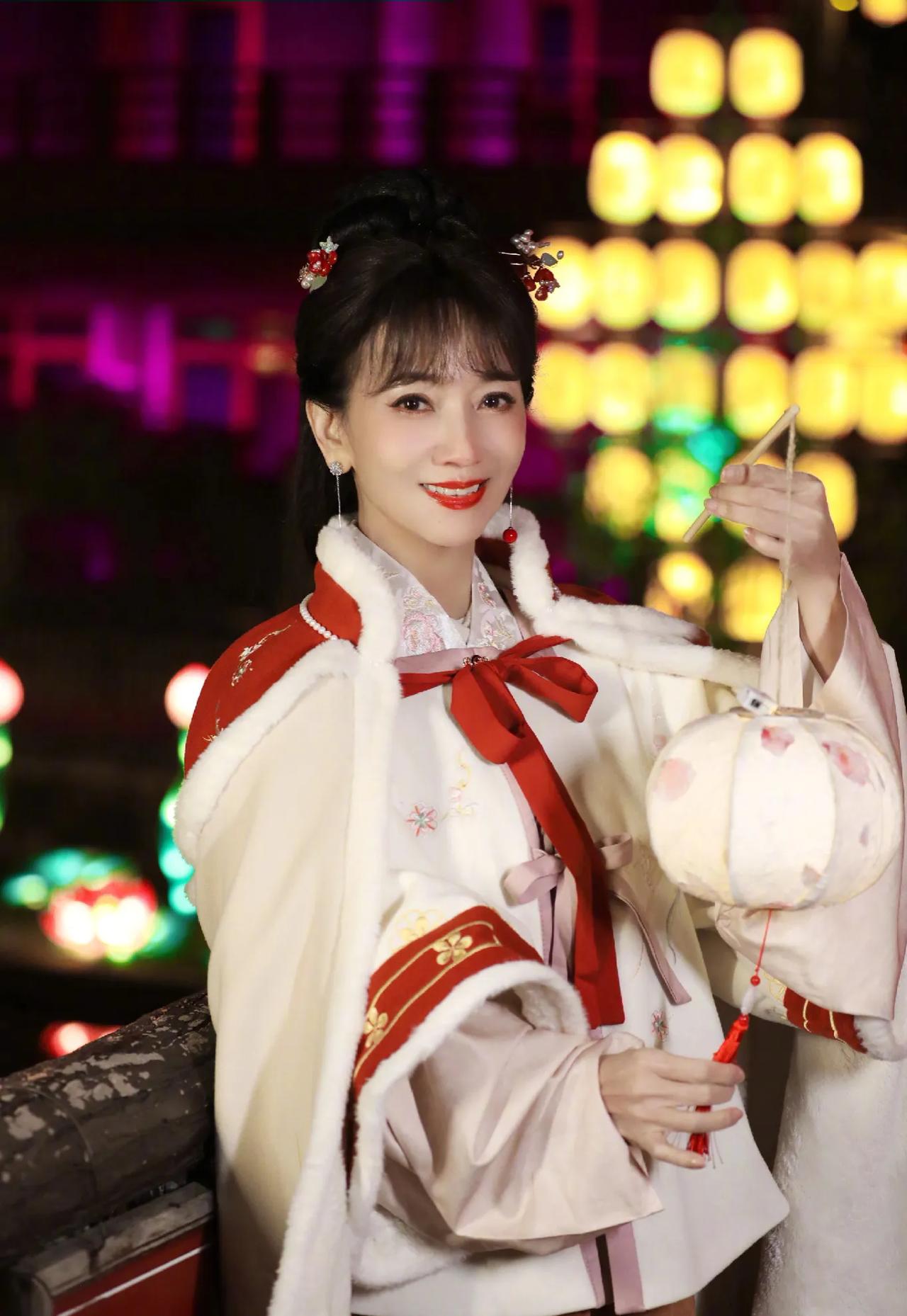 70岁赵雅芝穿汉服在江边拍照，这是要美一辈子啊！披着红色斗篷，手里举着花灯，十分