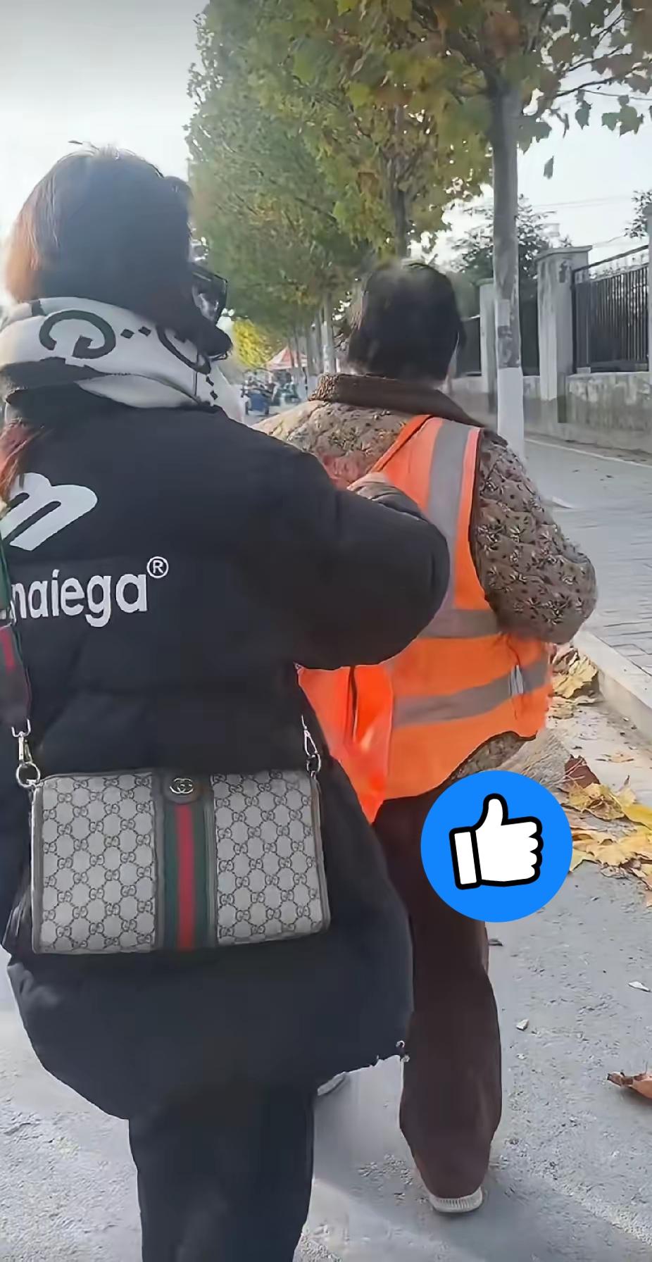 环卫工阿姨正在清扫地上的落叶，一名年轻女子突然走过去脱掉了阿姨身上的工作服，路人