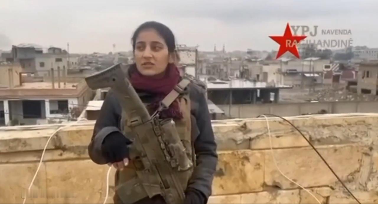 一名YPJ女战士站在拉卡的一处屋顶上，手持一支CZ BREN 2 BR突击步枪，