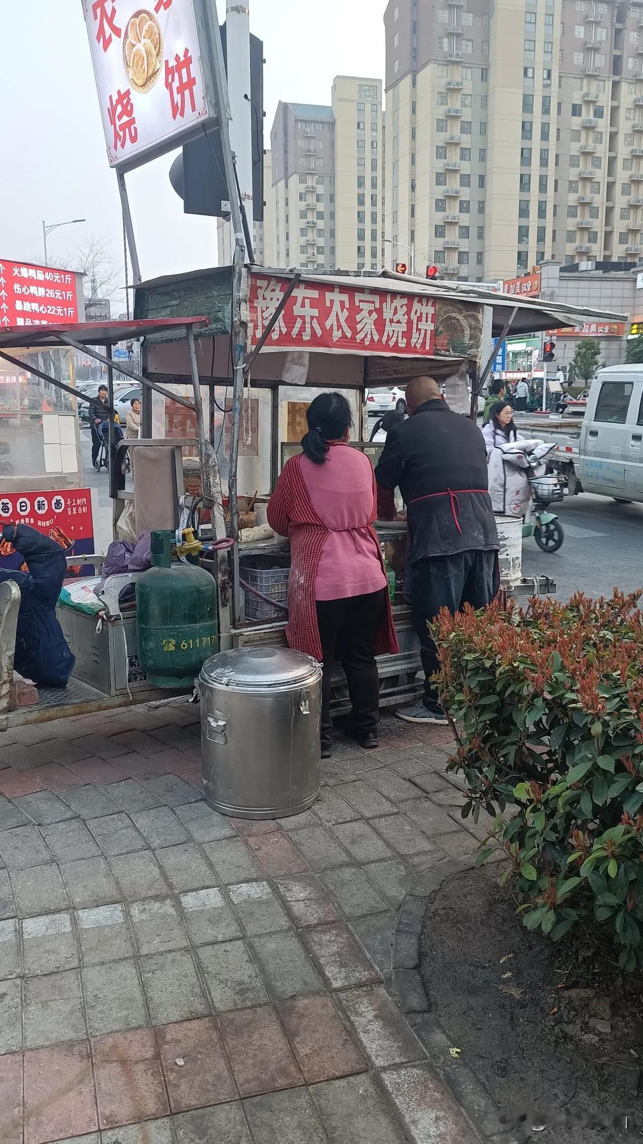 小区门口有两对农民夫妻摆摊卖烧饼，两个摊位一家在马路北边一家在马路南边，相距仅有