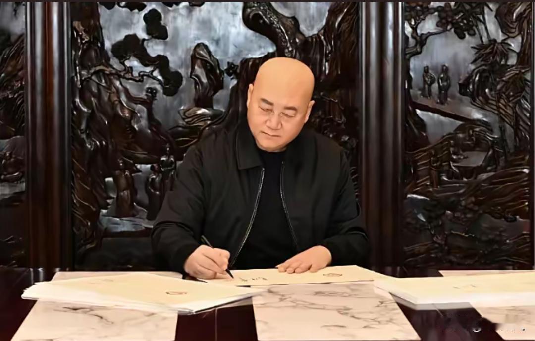 迟重瑞身后巨大雕花屏风是珍贵的紫檀木雕，他正在桌前书写。迟重瑞是国家一级演员，也