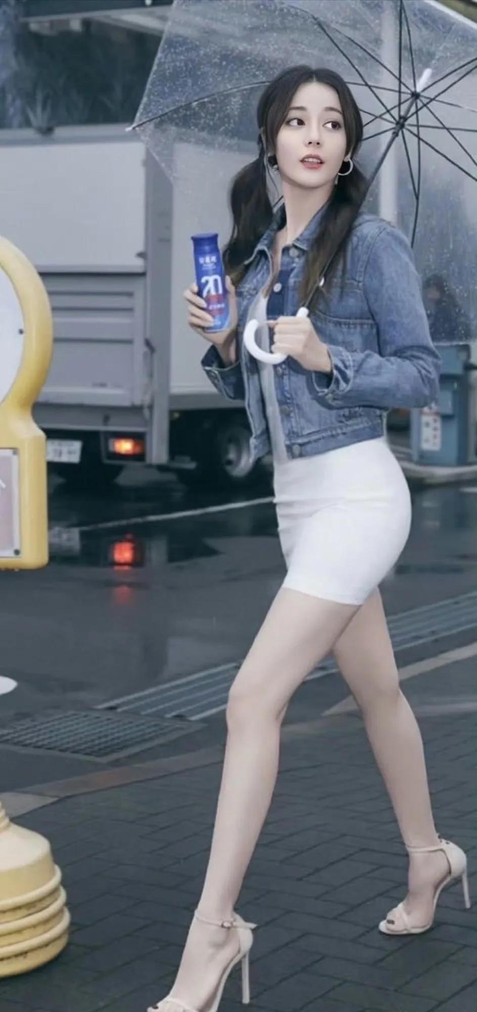 路人视角下的迪丽热巴，打着透明的油纸伞，穿着紧身白色短裙！脚穿一双浅色高跟凉鞋，
